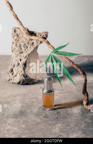 Glasflasche mit CBD-Öl, THC-Tinktur und Hanfblatt auf grauem Marmorboden. Minimalismus, Natürlichkeit. CBD-Öl-Kosmetik. Stockfoto