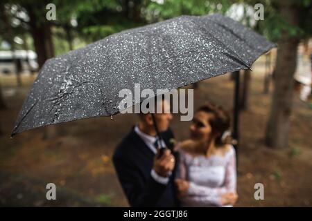 Regentropfen auf einem Regenschirm in den Händen des Brautpaten im Herbstwald. Die Idee eines Hochzeitsfotoshootings im Regen. Stockfoto