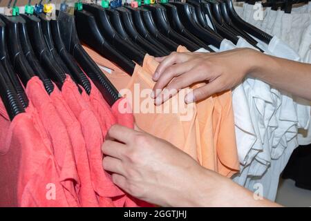 Der Käufer entscheidet sich für ein T-Shirt in einer Boutique. Gebrauchte Kleidung an Kleiderbügeln für Spenden und Wiederverkauf. Zweites Leben für Ihre Kleidung. Nachhaltiges Leben und Stockfoto