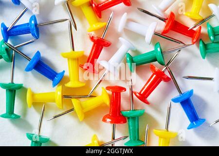 Farbige Schreibwarenknöpfe auf hellem Hintergrund. Nelken für die Ausbildung. Anbringen von Papier. Bürobedarf. Scharfer Stift zum Anbringen von Papier. Stockfoto