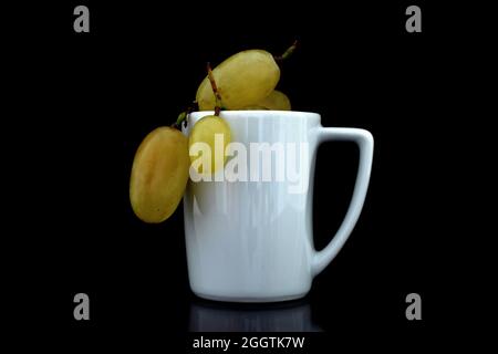 Mehrere Beeren von reifen süßen Trauben mit weißen Keramikschalen, Nahaufnahme, isoliert auf schwarz. Stockfoto