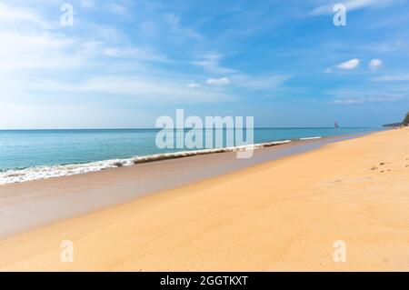 Goldgelber Sand an einem einsamen Strand in der Nähe des blauen Meeres an strahlendem Sonnentag. Kleines Boot, das im Hintergrund auf dem Meer segelt Stockfoto