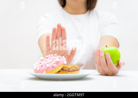 Slim Girl weigert sich, Donuts zu essen und beschließt, einen frischen Apfel zu essen, um Gewicht zu verlieren und fit zu bleiben. Stockfoto