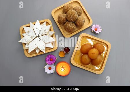 Diwali Diya, Süßigkeiten oder Mithai, und Blumen sind als festlicher Hintergrund angeordnet. Verschiedene Süßigkeiten Kaju Katli, Gulab Jamun und Churma laddu . Stockfoto