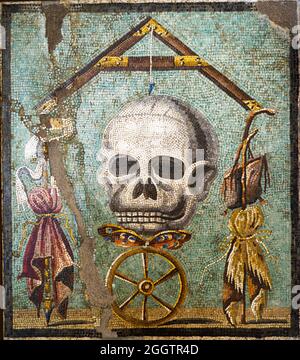 Memento Mori Mosaikemblema in opus vermiculatum aus polychromen Tesserae. Das Mosaik zeigt die Allegorie des Todes, die Unterschiede zwischen Menschen gleichstellt. Oben in der Komposition befindet sich ein Senklot mit seiner Senklinie, dessen Achse der Tod in Form eines Schädels ist; darunter befindet sich ein Schmetterling, die Seele, auf einem Rad, der das Glück symbolisiert: Zwischen den Armen des Klempnerblütlers befinden sich rechts die Symbole der Armut (Satteltasche, Bettelstab und Mantel) und links die Symbole des Reichtums (Zepter, Purpur und Krone). Pompeji, casa bottega (Geschäftshaus) - Italien Stockfoto