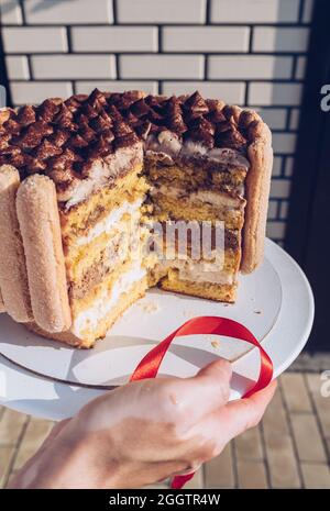Womans Hände halten geschnitten Tiramisu Kuchen an sonnigen Tag im Freien Stockfoto