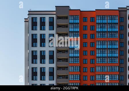 Neues Hochhausgebäude mit mehreren Balkons und Fenstern am blauen Himmel mit weißem Wolkenhintergrund. Stockfoto