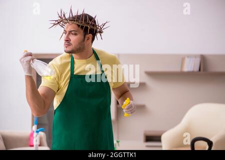 Junger männlicher Auftragnehmer, der auf dem Kopf einen stacheligen Kranz trägt und Hausarbeit leistet Stockfoto