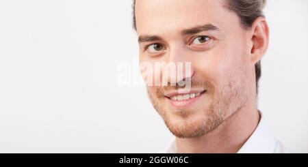 Nahaufnahme des jungen, gutaussehenden Mannes mit Bart, fröhlich lächelnd und in die Kamera schauend. Mann posiert in drei Vierteln. Foto mit Kopierbereich. Hor Stockfoto