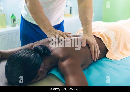 Frau bekommt eine Massage. Eine Physiotherapeutin macht eine Rückenmassage für eine schwarze Frau. Konzept der Massage-Spa-Behandlungen. Stockfoto