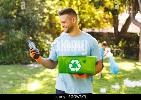 Lächelnder Kaukasusmann hält eine Recycling-Box und säubert die Landschaft mit gelaunter Laune Stockfoto