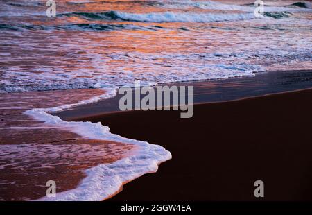 Wellen aus dem Atlantischen Ozean reflektieren das Licht der Sonne, wenn sie über dem Whitepark Bay Beach an der nordirischen Antrim Coast aufgehen. Stockfoto