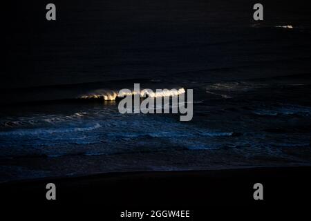 Wellen aus dem Atlantischen Ozean reflektieren das Licht der Sonne, wenn sie über dem Whitepark Bay Beach an der nordirischen Antrim Coast aufgehen. Stockfoto