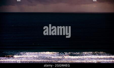 Wellen aus dem Atlantischen Ozean reflektieren das Licht der Sonne, wenn sie über dem Whitepark Bay Beach an der nordirischen Antrim Coast aufgehen. Stockfoto