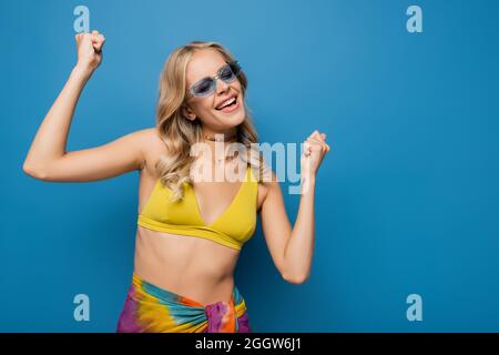 Aufgeregt junge Frau in trendigen Sonnenbrillen jubeln isoliert auf blau Stockfoto