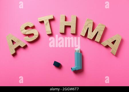 Word Asthma aus Holzbuchstaben und Inhalator auf rosa Hintergrund Stockfoto