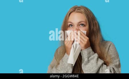 Junge blonde Frau, die an einer Allergie auf hellblauem Hintergrund leidet. Symptome von Erkältung oder Allergie. Frau niest in weißem Gewebe. Stockfoto