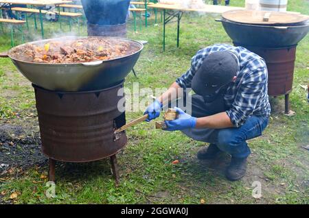 Kessel voller Reispilaf auf einem beweglichen Holzherd. Der Mensch legt ein Stück Holz in einen Ofen. Feier des Ramadan, Bruch des Fastens. Ma Stockfoto