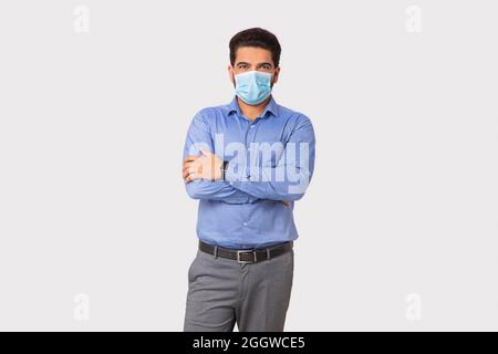 Porträt eines Mannes mit Maske auf Gesicht stehend mit Händen gekreuzt vor einfachem Hintergrund. Stockfoto