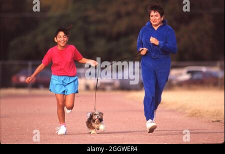 ©Austin Texas USA, 1991: Die hispanische Mutter und ihre 10-jährige Tochter joggen mit ihrem Hund auf einer Nachbarschaftsschulstrecke. ©Bob Daemmrich Stockfoto