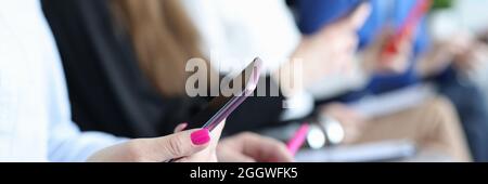 Frau, die auf einem Stuhl sitzt und das Telefon in den Händen hält Vor dem Hintergrund der Nahaufnahme von Kollegen Stockfoto