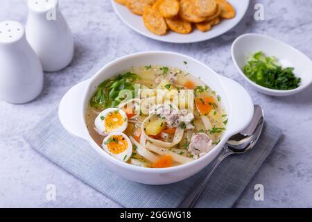 Suppe mit Hühnchen, Nudeln, Kartoffeln, Wachteleiern und Karotten. Gewürzt mit Zwiebeln und Petersilie. Nahaufnahme. Stockfoto