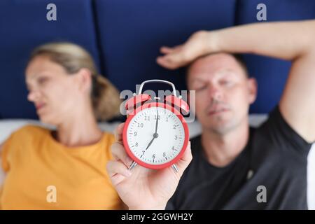 Schlafender Mann und Frau liegen im Bett und halten den roten Wecker in der Nähe Stockfoto