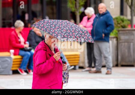 Dundee, Tayside, Schottland, Großbritannien. September 2021. Britisches Wetter: Ein sehr kalter und bewölktes Tag mit gelegentlichen leichten Schauern in Nordostschottland mit Temperaturen bis zu 14 Grad Anwohner genießen den Tag im Freien nach monatelangen Coronavirus-Sperren. Eine ältere Frau, die sich unter einem Brülligen unterm Hotel unterm Einkaufsbummel in den sehr kalten und langweiligen Bedingungen im Stadtzentrum von Dundee unterm Hotel aufhalten kann. Kredit: Dundee Photographics/Alamy Live Nachrichten Stockfoto