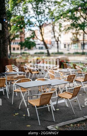 Stühle und Tische in einem Restaurant im Freien mit bunten Glühbirnen zwischen Bäumen Stockfoto