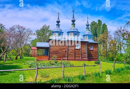 Der grüne Rasen und der kleine Garten rund um die alte Holzkirche, in Pereiaslav Scansen, Ukraine Stockfoto