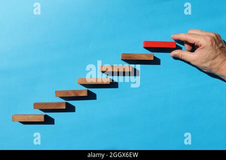 Männliche Hand hält oben roten Holzblock auf blauem Hintergrund Stockfoto