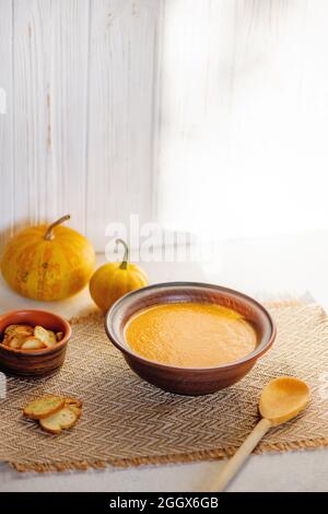 Kürbissuppe in Keramikschale auf weißem Holzhintergrund. Stockfoto