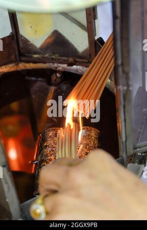 Die Hand einer Frau zündete Räucherstäbchen an einer Öllampe in einem Schrein, um für die Götter zu beten. Asiatische Überzeugungen religiöse Zeremonie. Stockfoto