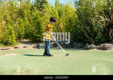 Ein kleiner Junge spielt an einem sonnigen Tag verrücktes Golf. Stockfoto