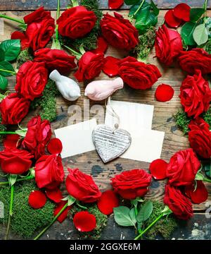 Rote Rosen, zwei Vögel, Papierkarten und weißes Herz auf Holzgrund. Stockfoto