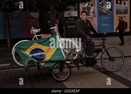 Dublin, Irland. September 2021. Ein Mann fährt mit seinem Fahrrad die Hauptstraße Dublins entlang und trägt ein weiteres weißes Fahrrad mit einer brasilianischen Flagge, die während des Tributs angebracht ist.Thiago Cortes, ein brasilianischer Radfahrer und Deliveroo-Fahrer, wurde vor einem Jahr von einem Teenager bei einem Unfall getötet, als er auf seinem Fahrrad Lebensmittel lieferte. Der Teenager wurde zu zwei Jahren Gefängnis verurteilt. Wenige Tage nach dem tragischen Unfall im Jahr 2020 fand auf den Straßen Dublins eine große Mahnwache und ein Marsch zum Gedenken an Thiago statt. (Foto von Natalia Campos/SOPA Images/Sipa USA) Quelle: SIPA USA/Alamy Live News Stockfoto