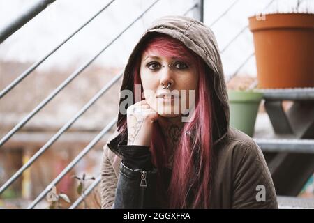 Nachdenkliche junge Frau mit Piercings und Tattoos auf der Außentreppe Stockfoto