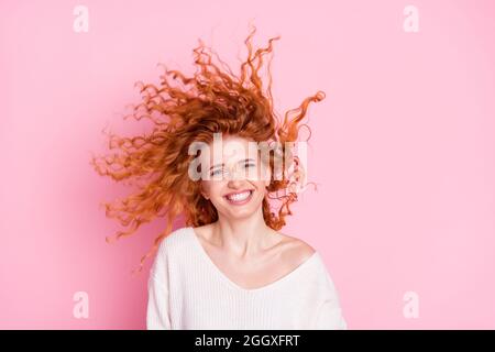 Foto-Porträt von jungen Mädchen lachen mit Haaren fliegen in der Luft tragen weißen Pullover isoliert pastellrosa Farbe Hintergrund Stockfoto