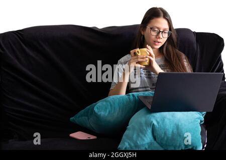 Frau, die auf ihrem Sofa sitzt und Kaffee trinkt. Frau, die auf ihrem Laptop studiert Stockfoto