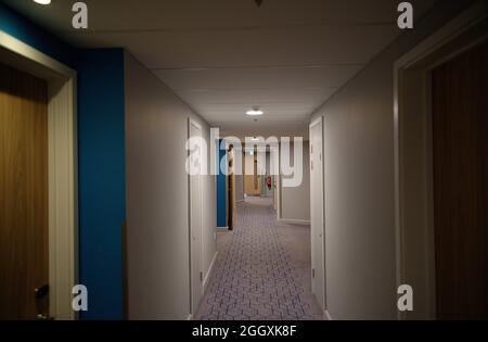 Ein schwach beleuchteter Hotelkorridor mit schlichten Wänden und einem gemusterten Teppich. Stockfoto