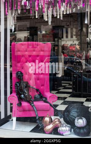 Lviv, Ukraine, Oktober 2018: Ein farbenfrohes Halloween-Display in einem Schaufenster in Lviv. Menschliches schwarzes Skelett sitzt in einem Pink Velvet Stuhl. Stockfoto