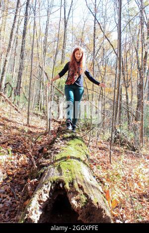 Rothaarige Frau, die auf einem Holzbalken im Wald in den Bergen läuft und versucht, das Gleichgewicht zu finden Stockfoto