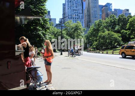 Menschen, die vor dem Central Park Schlange stehen und darauf warten, Snacks und Wasser zu kaufen. Eine Pferdekutsche fährt vorbei, und die Leute reiten auf ihr. Stockfoto