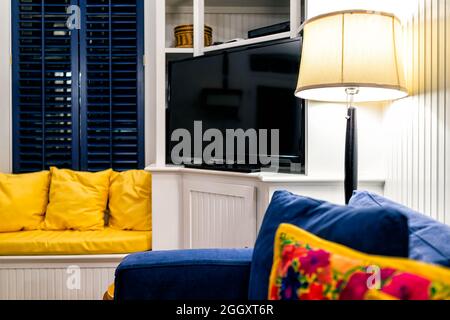 Moderne Wohnzimmersofas mit dunklem Fenster in der Nacht und blaue Couch durch beleuchtete Lampe und Fernseher mit niemand im Haus Stockfoto
