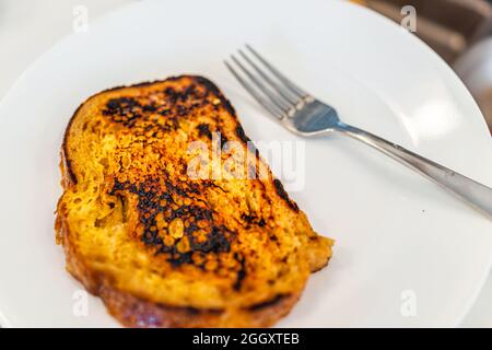 Nahaufnahme von hausgemachtem, gekochtem Challah Brioche-Brot, französischem Toast, gebraten auf weißem Teller mit Gabel und verbranntem Essen Stockfoto