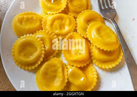 Gelbe orange Kürbis oder Zitrone Ravioli Italienische runde Form Pasta mit Ricotta-Käse Füllung auf weißem Teller gekocht und Gabel oben closeup Stockfoto