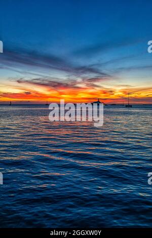 Silhouetten von Booten bei farbenprächtiger Dämmerung blaue Stunde mit Blick auf die Landschaft auf blau bewölkten Himmel Reflexion im Wasser durch Mallory Square von Key West, F Stockfoto