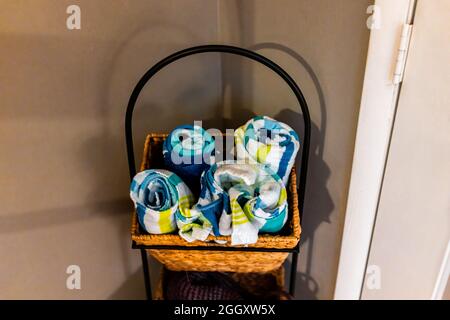 Rollen von gefalteten bunten Baumwolle Strandhandtücher Rollen in Korbkorb stehen im Haus Zimmer innen durch eine Wandtür in der Ecke Stockfoto