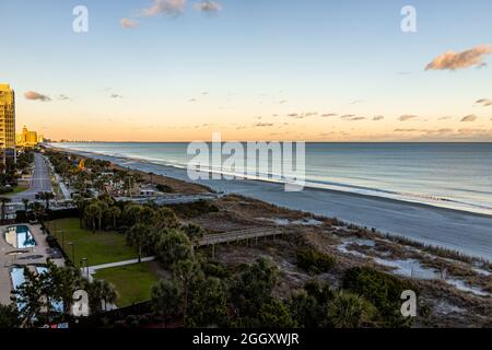 Luftaufnahme aus dem hohen Winkel auf Myrtle Beach Stadt am Atlantik bei Sonnenuntergang mit Strandzugang auf der Promenade und vielen Wohnungen am Meer am Strand Stockfoto