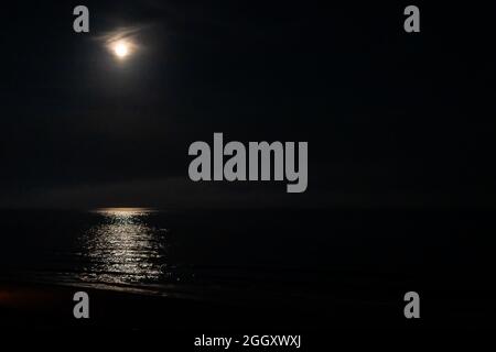 Großer Vollmond, der in dunkler Nacht über dem Atlantik aufsteigt, mit Mondlichtweg, der sich auf dem Wasser mit Wolken in Myrtle Beach, South Carolina, widerspiegelt Stockfoto